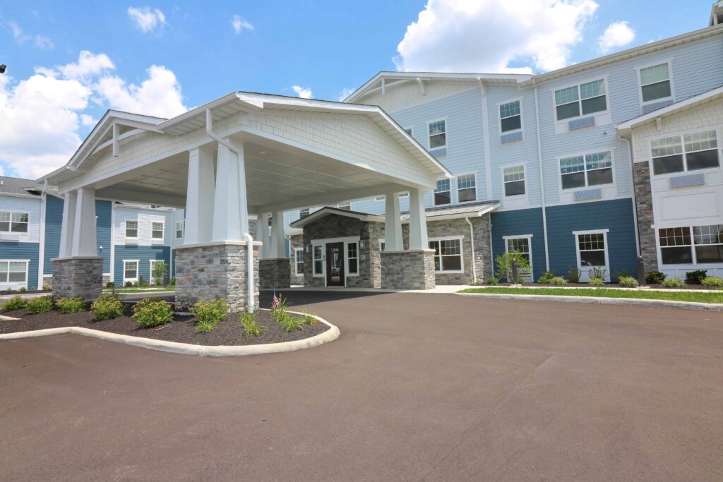 the stone, white and blue exterior of the Traditions at North Bend senior living building, featuring a shaded carport