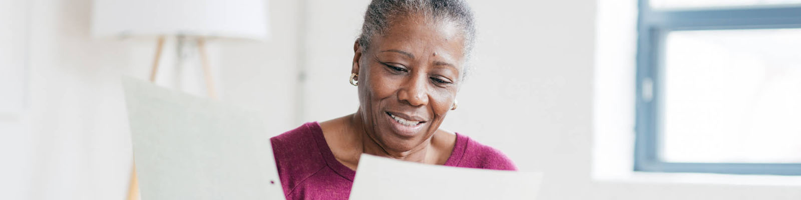 A senior woman wearing a purple shirt looking down at two documents she is holding