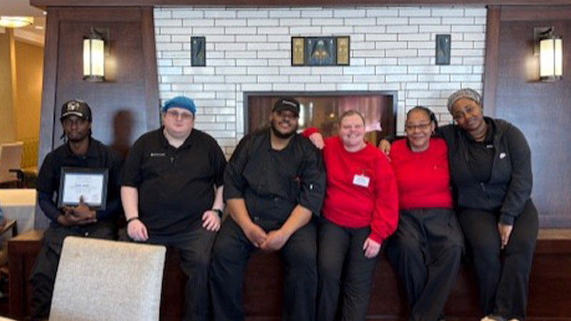 North Bend Senior Living culinary team gathered in front of a fireplace