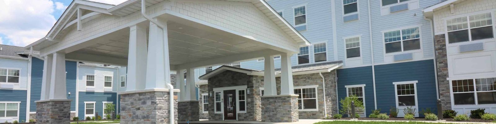 Covered front entrance of a three-story residential building with blue and white siding and stone accents